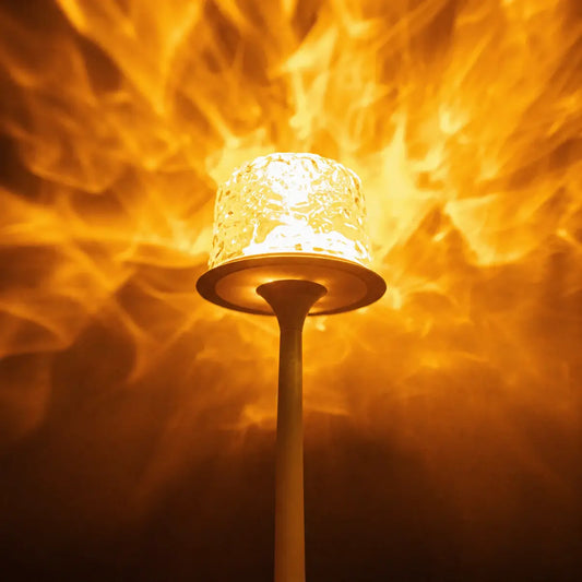 Close-up of a witlity skywave lamp with a rippled ice-crack glass shade, glowing with warm golden light. It casts flame-like flowing orange-gold light patterns on the background, paired with a smooth matte light-colored stem, highlighting the lamp's artistic light effect and creating a cozy warm atmosphere.