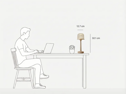 Minimalist black-and-white line art showing a table lamp's usage scene and size specs. A man sits on a wooden chair working on a laptop at a desk, with a small succulent and the Witlity's skywave lamp on the table. Marked with 32.1 cm total height and 12.7 cm shade diameter, it clearly presents the lamp's size proportion and desktop compatibility.