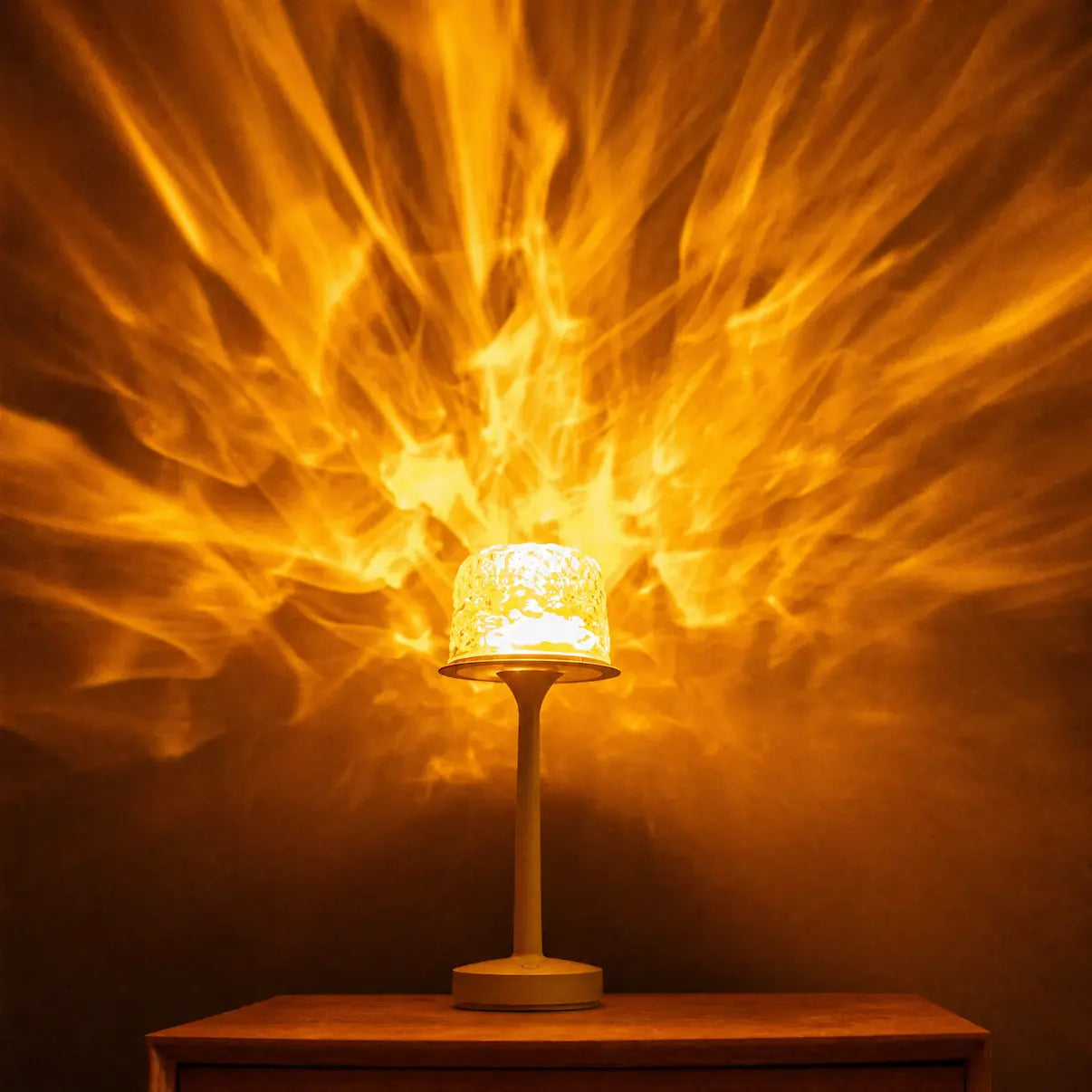 A witlity skywave lamp with a clear rippled ice-crack glass shade emits warm golden light, casting vibrant flame-like flowing orange-gold radial patterns. With a smooth matte light-colored stem resting on a wooden table against a dark background, it creates a warm, cozy, highly atmospheric relaxing home ambiance.