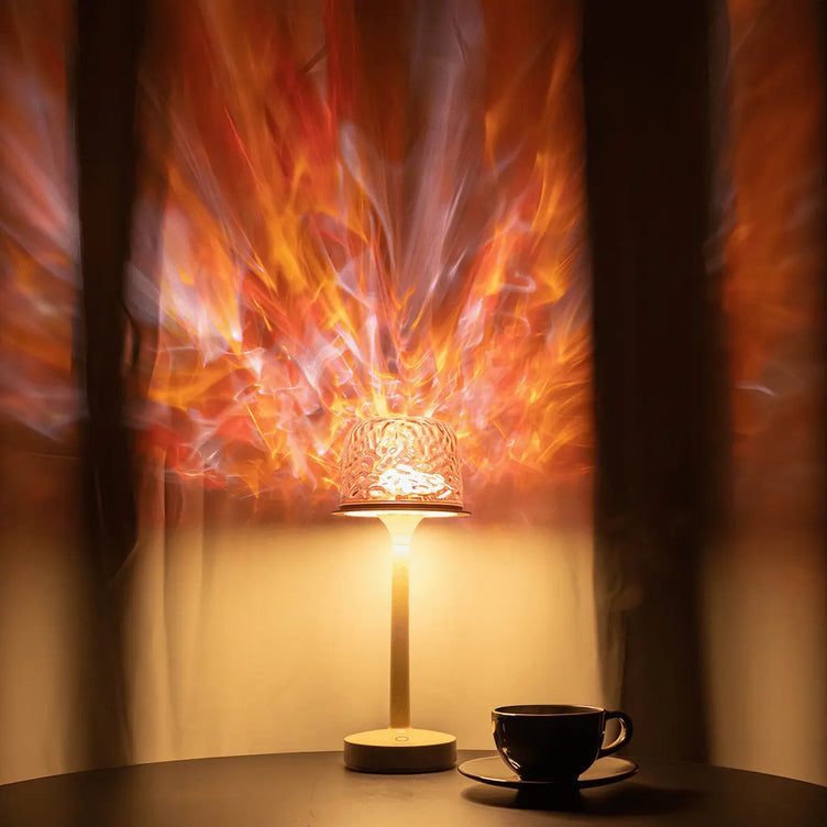 Warm-toned home scene: a witlity skywave lamp with rippled ice-crack glass shade casts flame-like flowing orange-red radial light patterns, paired with a black ceramic cup and saucer on the table, creating a cozy, relaxing, highly atmospheric ambiance against soft curtains.